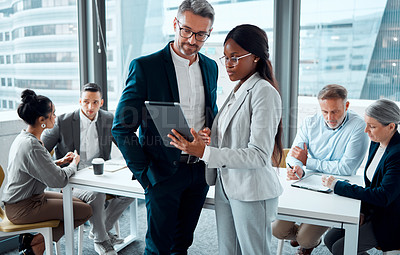 Buy stock photo Shot of two businesspeople using a digital tablet in an office with their colleagues in the background