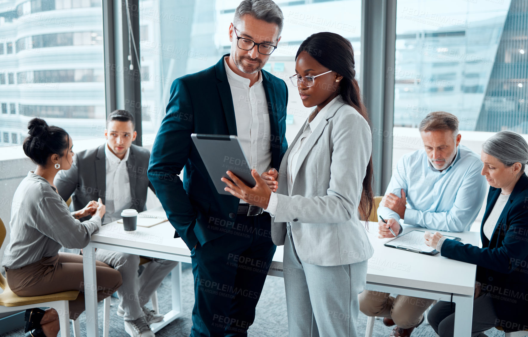 Buy stock photo Shot of two businesspeople using a digital tablet in an office with their colleagues in the background