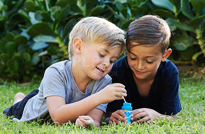 Buy stock photo Shot of two adorable boys playing with bubbles on the grass in the backyard