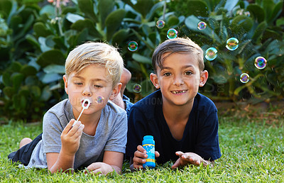 Buy stock photo Friends, playing and children blowing bubbles in park for weekend activity, bonding or having fun together. Happy, relax and young boys lying on lawn for childhood, leisure or enjoyment in backyard