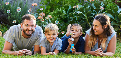 Buy stock photo Portrait of a beautiful family laying on the grass and playing with bubbles in a backyard