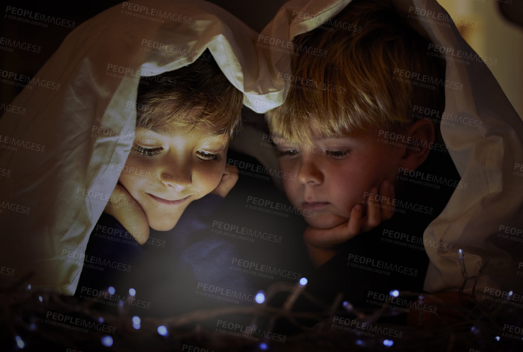 Buy stock photo Shot of two adorable little boys using a digital tablet under a blanket fort at night in their bedroom