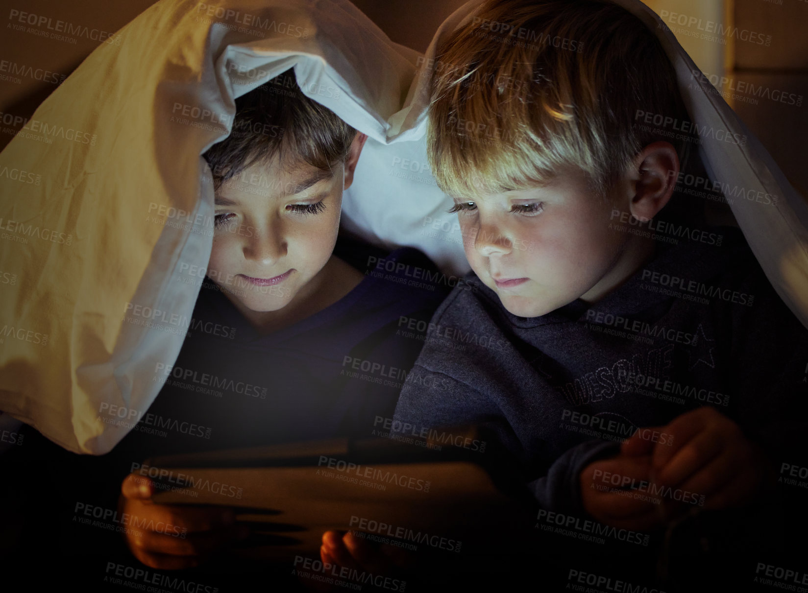 Buy stock photo Shot of two adorable little boys using a digital tablet under a blanket fort at night in their bedroom