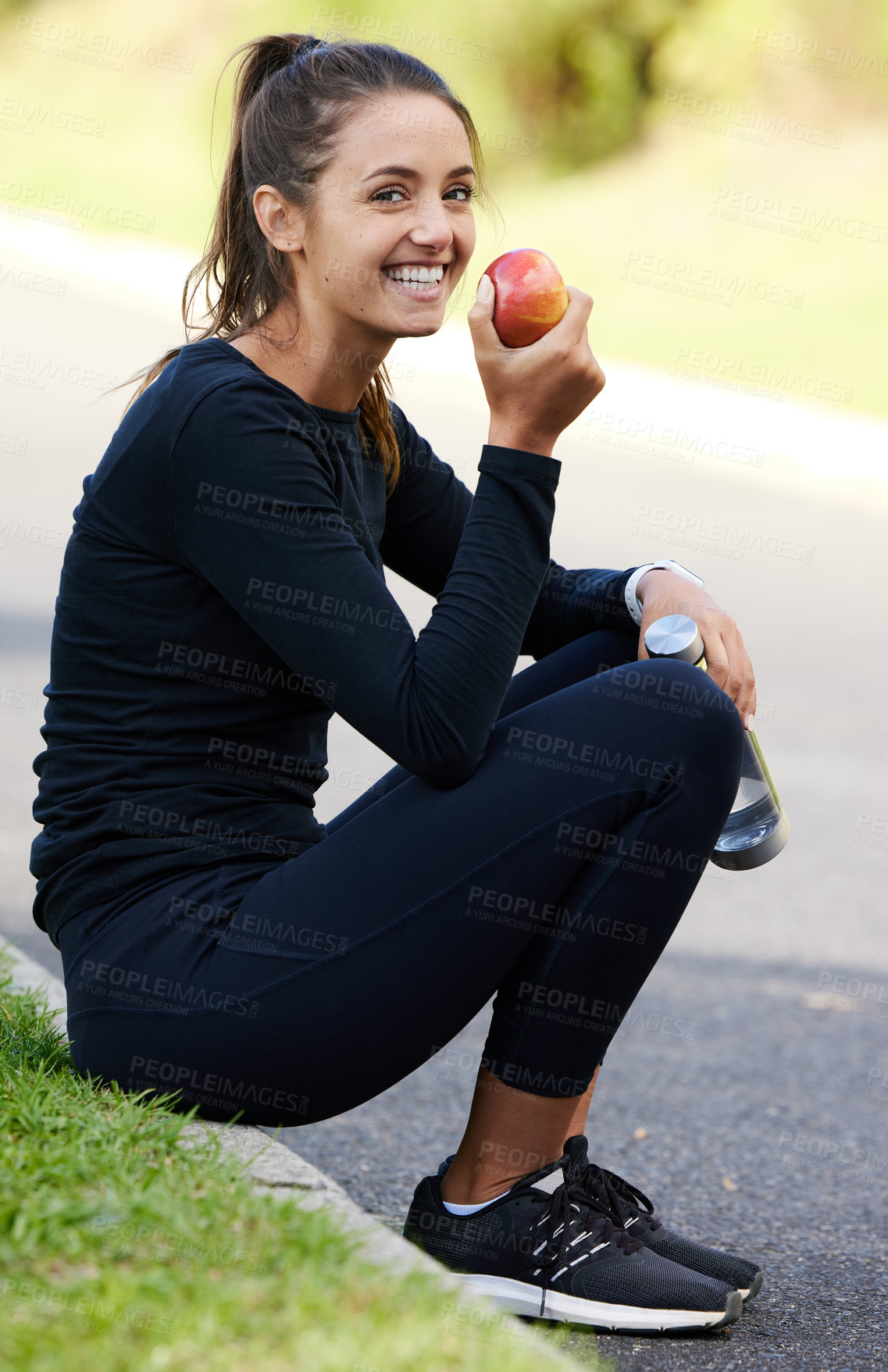 Buy stock photo Full length portrait of an attractive and athletic young woman sitting on the curb with her apple and water bottle