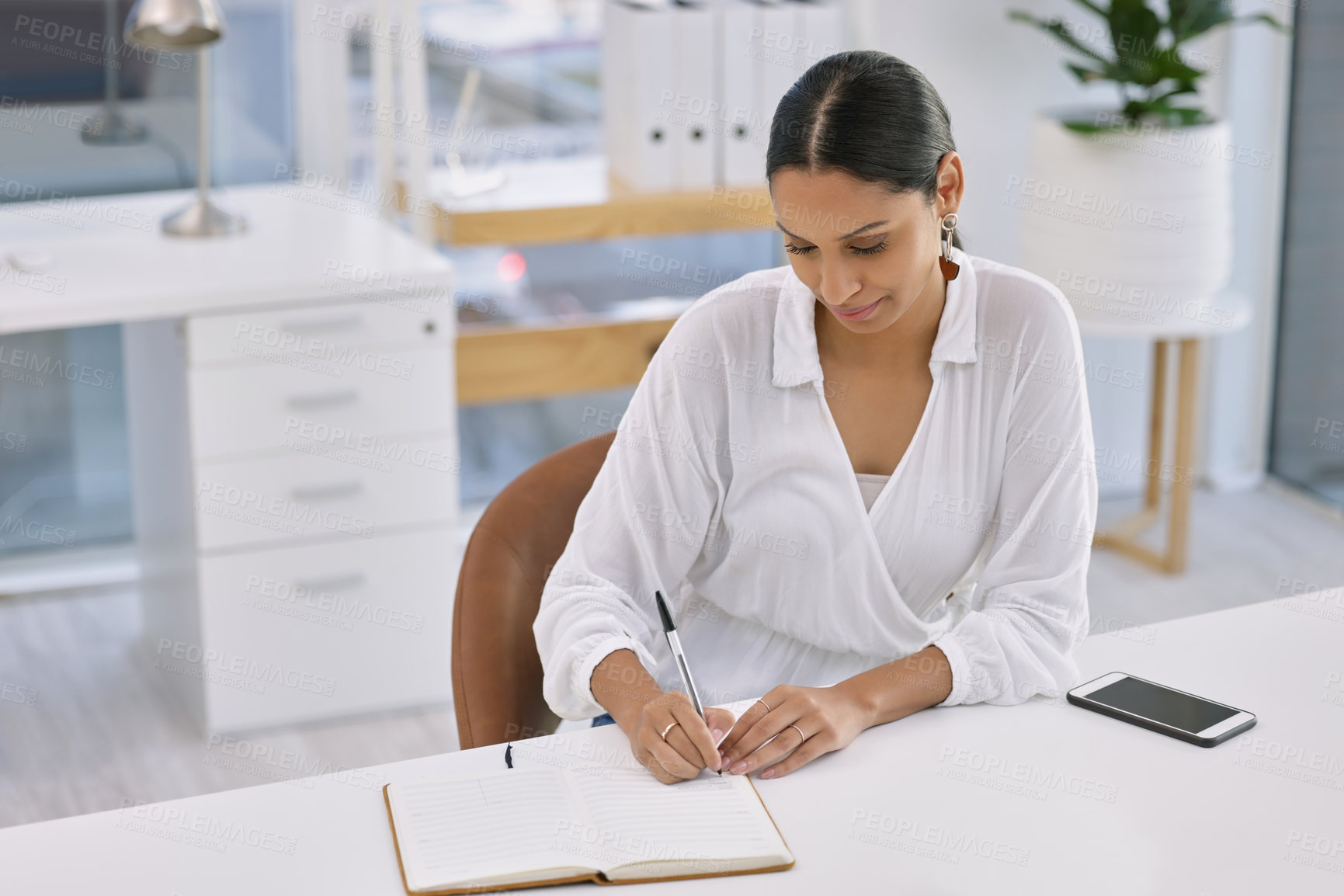 Buy stock photo Shot of a businesswoman writing in a book in a modern office