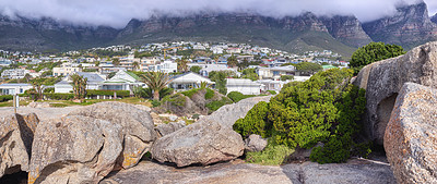 Buy stock photo Rocks and boulders against a majestic mountain and cityscape background with lush green plants and coulds. Remote and quiet landscape on a cliff with stones to enoy a urban view with private homes