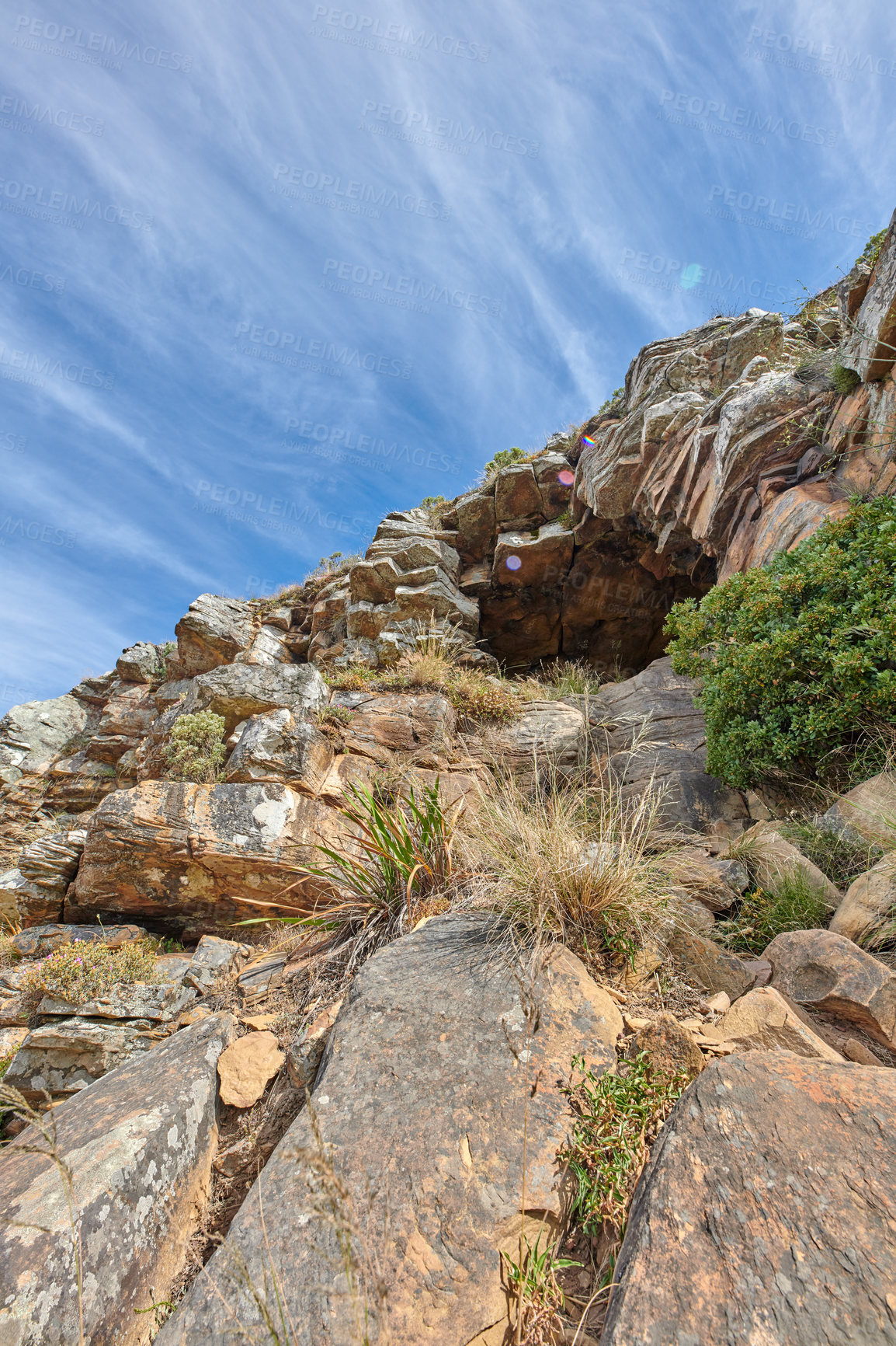 Buy stock photo Cliff at the side of mountain or island with cave to rest in after rock climbing, surrounded by plants, trees and nature in summer or spring. Closeup view from the bottom of a canyon with a blue sky