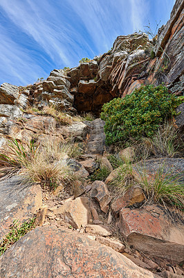 Buy stock photo A rocky mountain with plants and shrubs growing against a cloudy sky background with copy space. Rugged, remote and quiet landscape with rocks and stones on a cliff leading to a mysterious cave