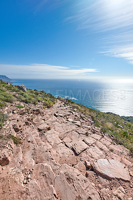 Buy stock photo Mountain trail to beautiful big ocean blue sky. Adventure through, rocky trails and greenery surrounded by the elements of nature. Sunny day in rock, grass and water environment in the outdoors.