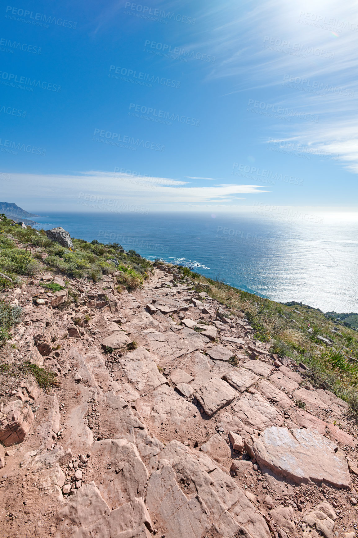 Buy stock photo Mountain trail to beautiful big ocean blue sky. Adventure through, rocky trails and greenery surrounded by the elements of nature. Sunny day in rock, grass and water environment in the outdoors.