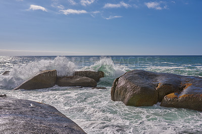 Buy stock photo A beautiful coastline with waves and rocks in the sea on a sunny, beach day. An ocean view of the water and a blue sky background in summer. Outdoor scenery of a relaxing seaside landscape in nature.