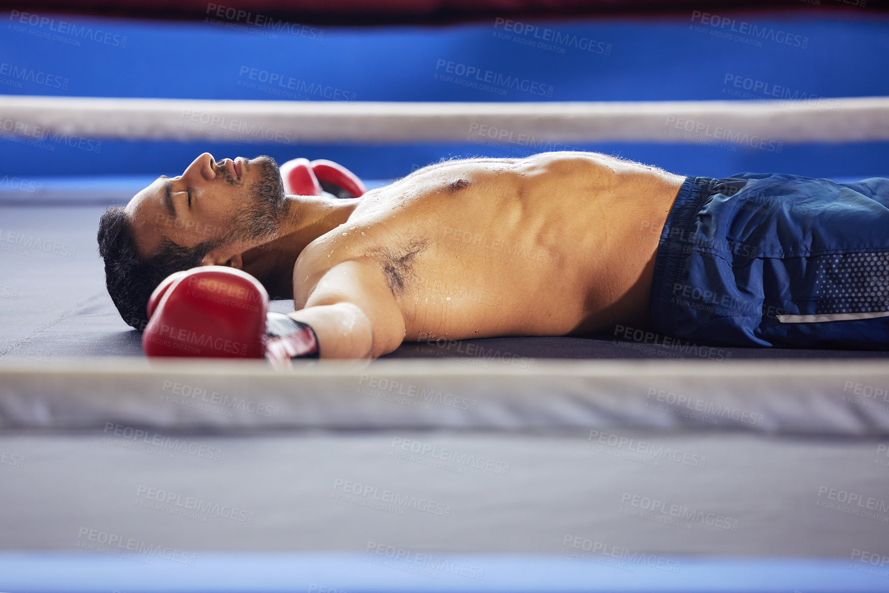 Buy stock photo Cropped shot of a handsome young male boxer lying in the ring with his eyes closed after a fight