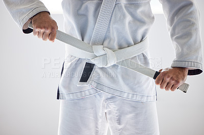 Buy stock photo Cropped shot of an unrecognizable male martial artist tying his belt in the gym