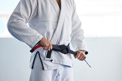 Buy stock photo Cropped shot of an unrecognizable male martial artist tying his belt in the gym