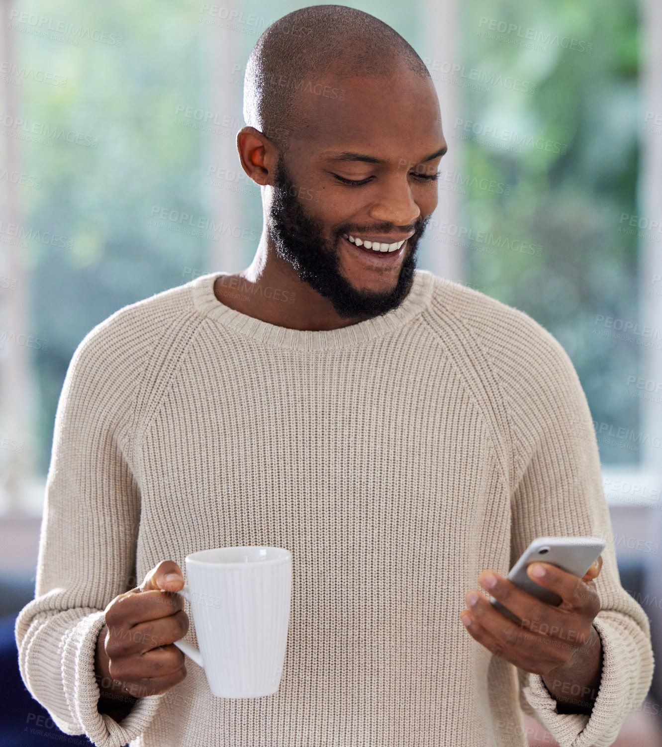 Buy stock photo Shot of a young man drinking coffee while using a phone at home