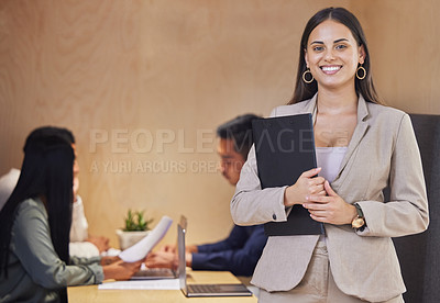 Buy stock photo Cropped portrait of an attractive young businesswoman standing with a clipboard in the boardroom with her colleagues in the background