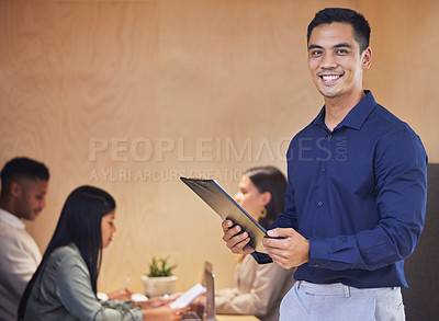 Buy stock photo Cropped portrait of a handsome young businessman standing with a clipboard in the boardroom with her colleagues in the background