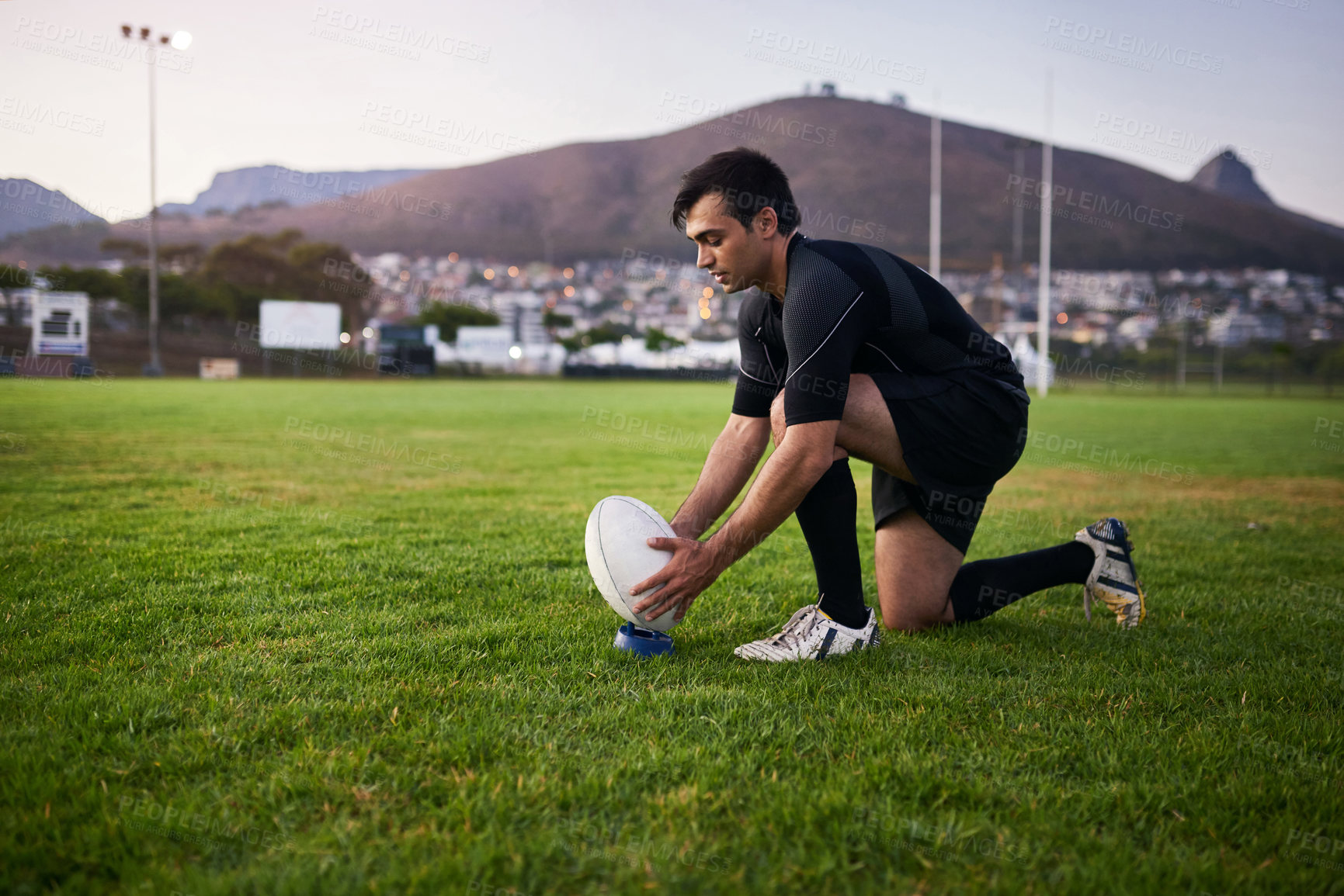 Buy stock photo Full length shot of a handsome young sportsman crouching alone during rugby practice in a sports club