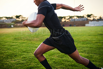 Buy stock photo Cropped shot of an unrecognizable sportsman running alone while holding a rugby ball during an early morning practice