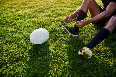 Buy stock photo Cropped shot of an unrecognizable sportsman sitting alone and tying his shoelaces before playing rugby during the day