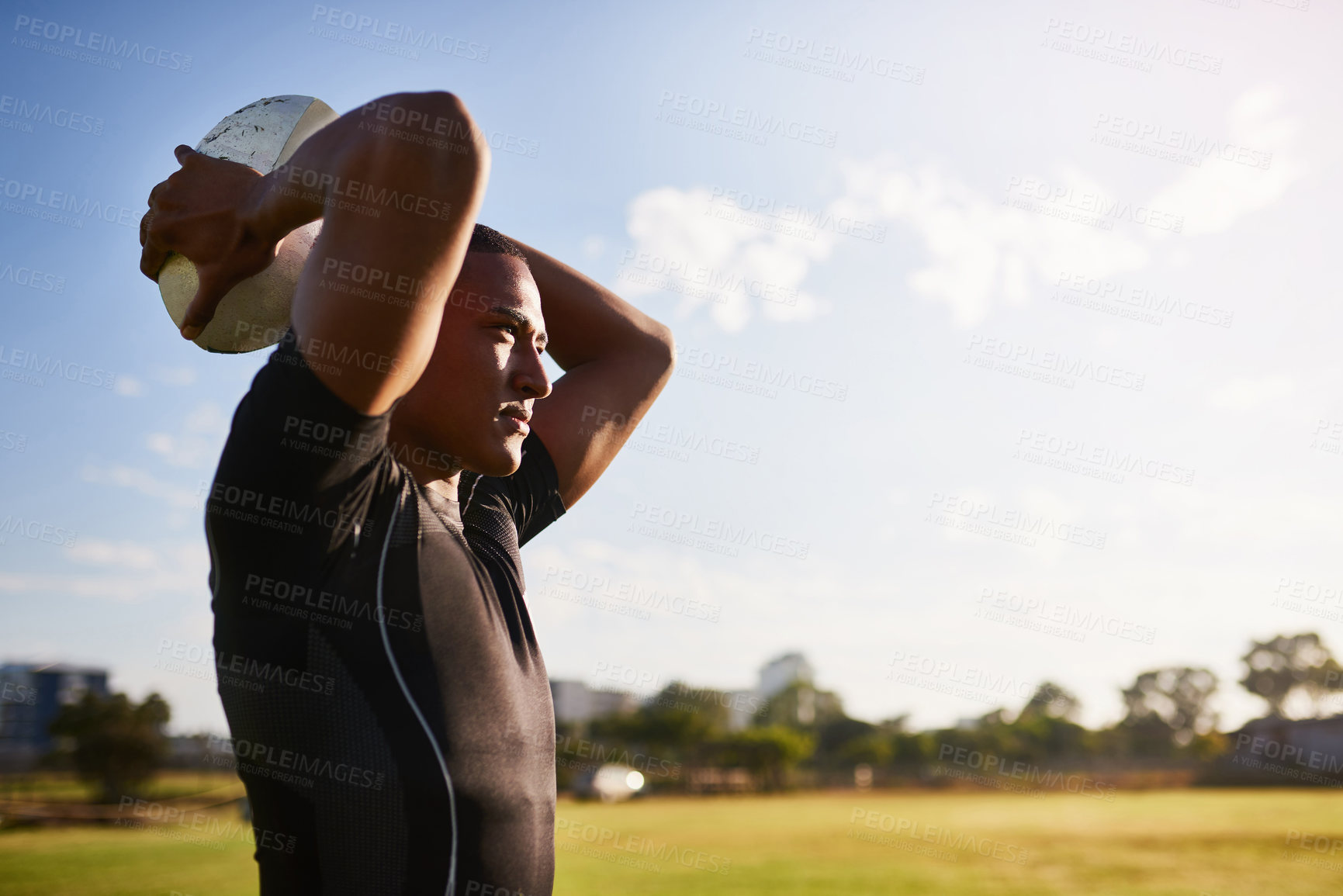 Buy stock photo Cropped shot of a handsome young sportsman standing alone and throwing a rugby ball during practice during the day