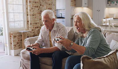 Buy stock photo Shot of a senior couple sitting on the sofa at home together and gaming