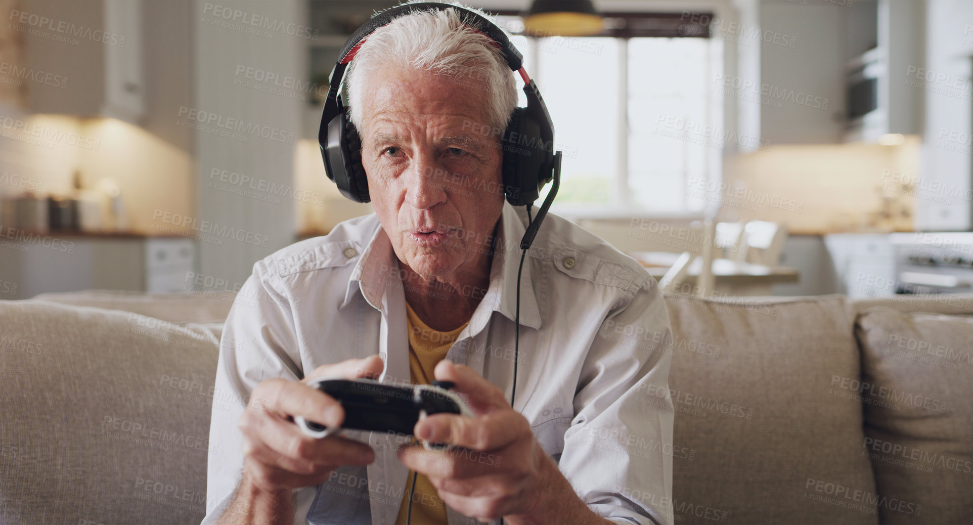 Buy stock photo Shot of a senior man sitting alone on the sofa at home and wearing headsets while gaming