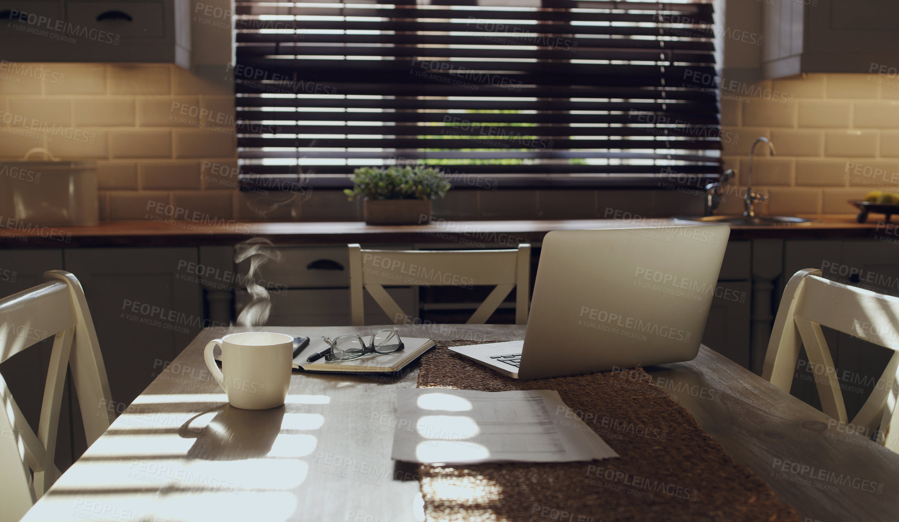 Buy stock photo Shot of a laptop and work supplies on a table in an empty kitchen during the day