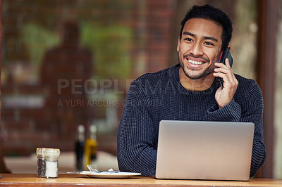 Buy stock photo Shot of a man talking on his cellphone and using his laptop while sitting in a cafe