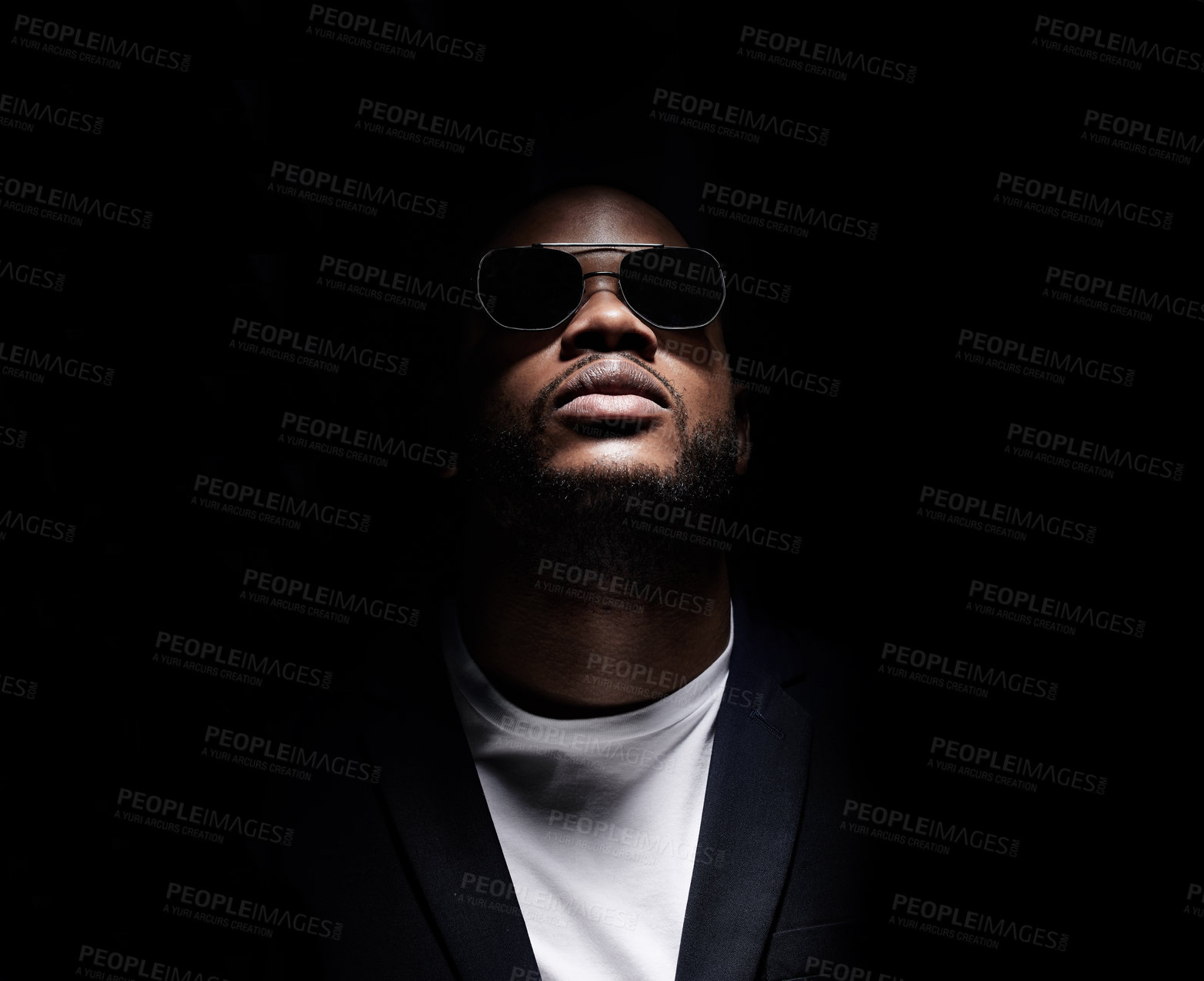 Buy stock photo Studio shot of a man wearing sunglasses while posing against a dark background