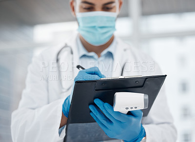 Buy stock photo Shot of a young doctor writing down information while holding a thermometer in an office