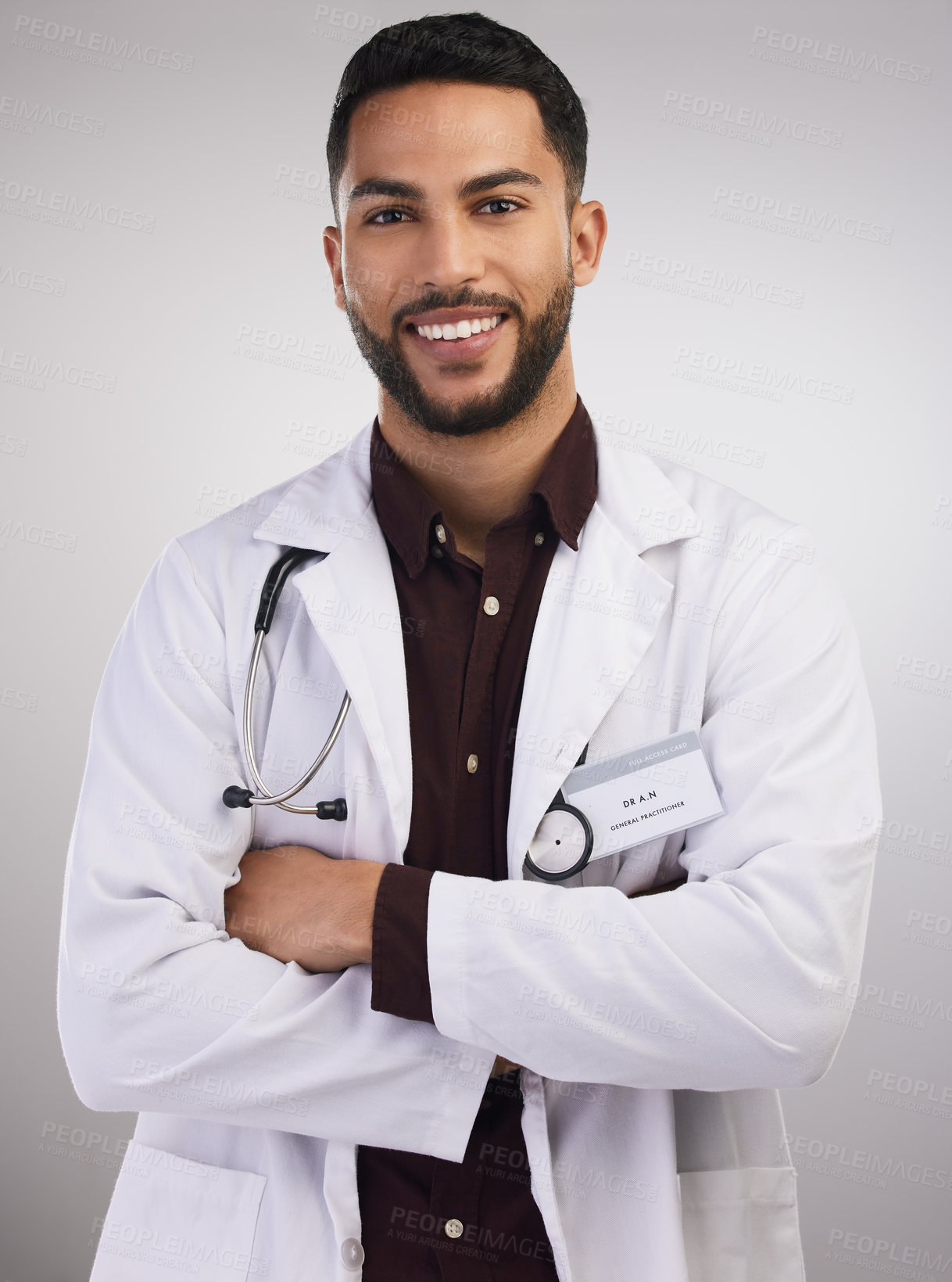 Buy stock photo Shot of a handsome young doctor standing alone in the studio with his arms folded