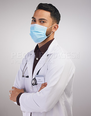 Buy stock photo Shot of a handsome young doctor standing alone in the studio with his arms folded and wearing a face mask