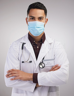 Buy stock photo Shot of a handsome young doctor standing alone in the studio with his arms folded and wearing a face mask
