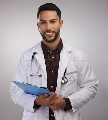 Buy stock photo Shot of a handsome young doctor standing alone in the studio and holding a clipboard