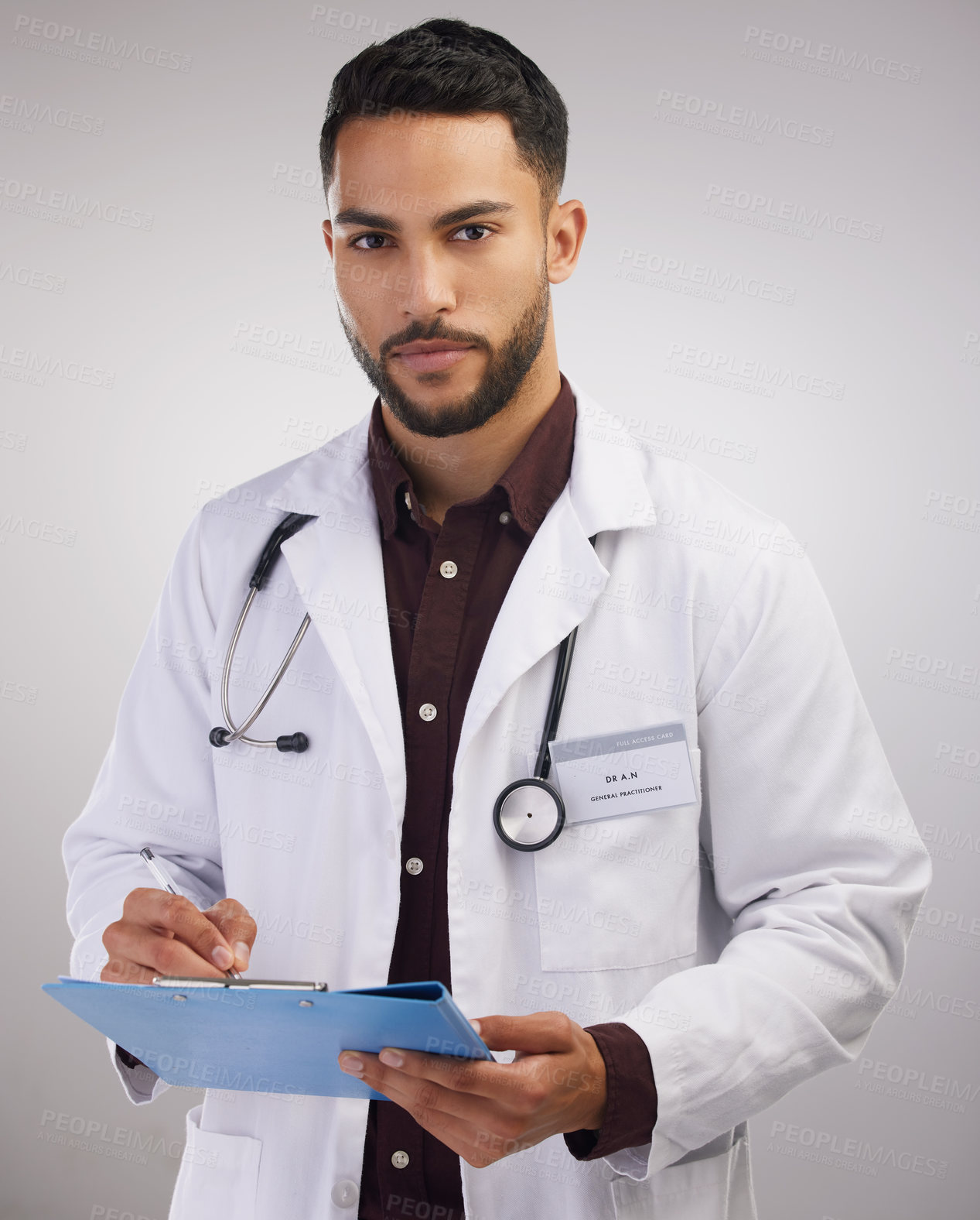 Buy stock photo Shot of a handsome young doctor standing alone in the studio and writing on a clipboard