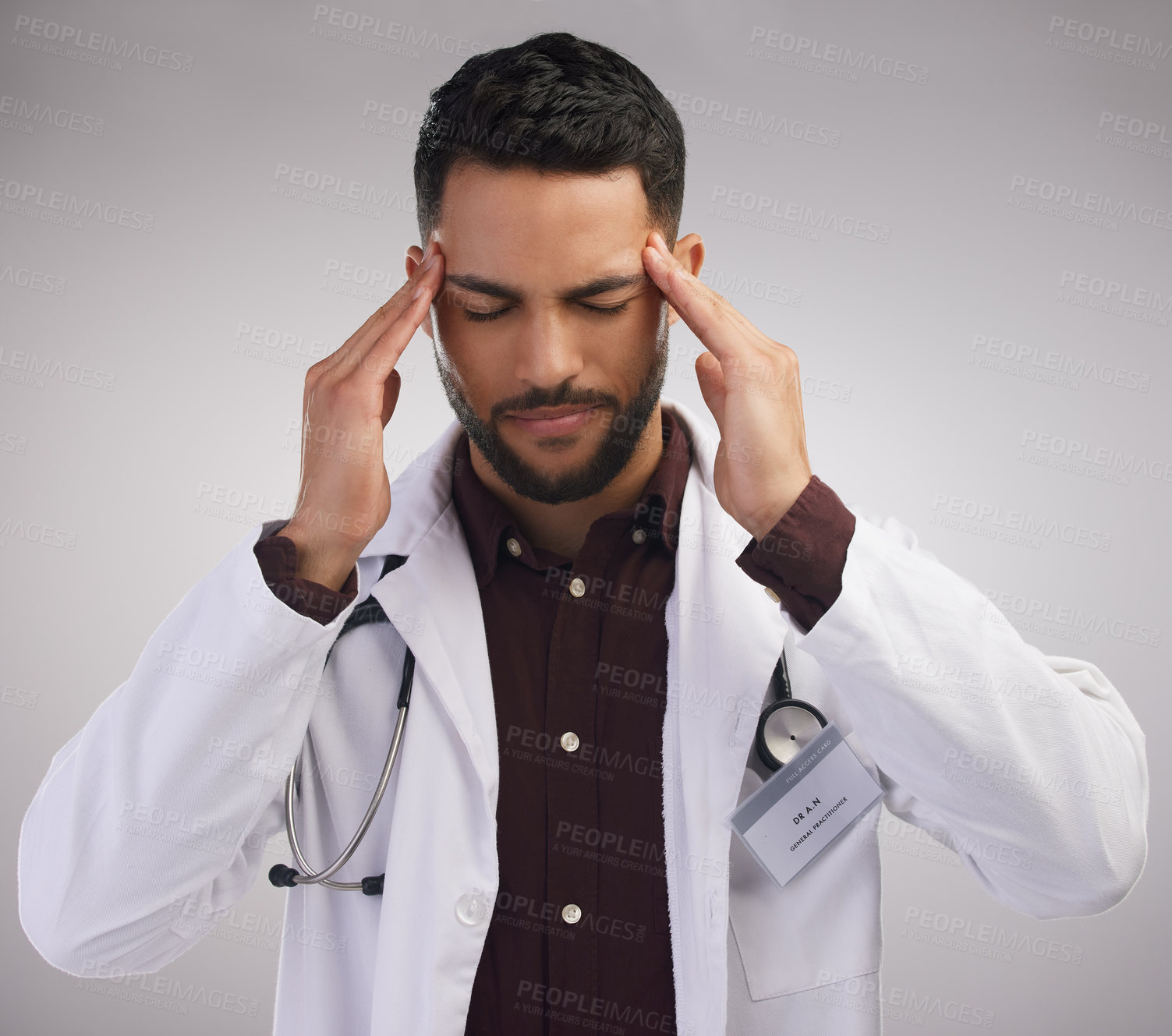 Buy stock photo Shot of a handsome young doctor standing alone in the studio and suffering from a headache