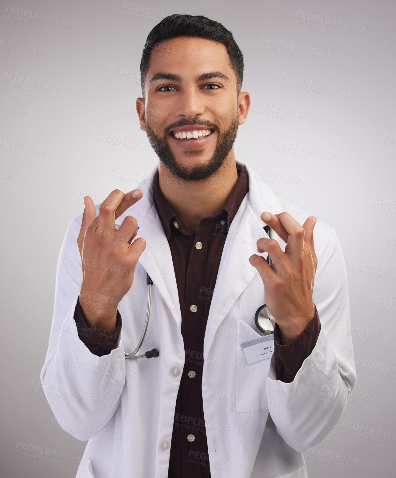 Buy stock photo Shot of a handsome young doctor standing alone in the studio with his fingers crossed for good luck