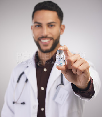 Buy stock photo Shot of a handsome young doctor standing alone in the studio and holding a vial of the Covid vaccine