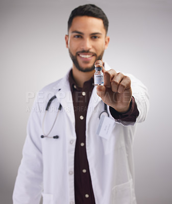 Buy stock photo Shot of a handsome young doctor standing alone in the studio and holding a vial of the Covid vaccine