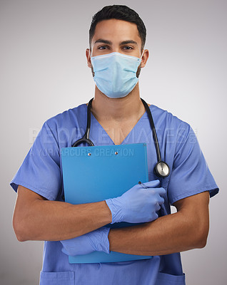 Buy stock photo Shot of a handsome young nurse standing alone in the studio and holding a clipboard while wearing a face mask