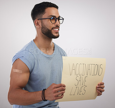 Buy stock photo Shot of a handsome young man sitting alone in the studio and holding a poster after getting vaccinated