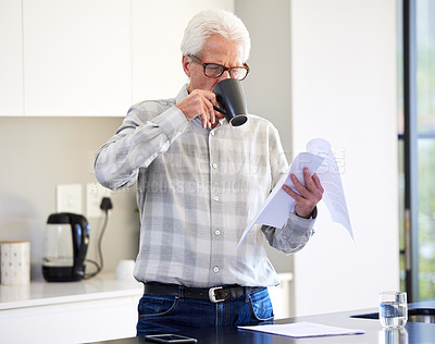 Buy stock photo Shot of a mature man reading paperwork while drinking tea
