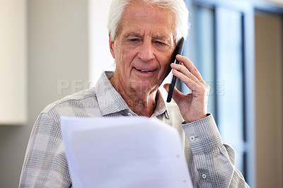 Buy stock photo Shot of a mature man reading paperwork while making a call