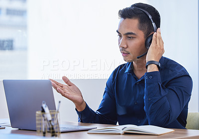 Buy stock photo Shot of a young businessman wearing a headset while using a laptop in an office