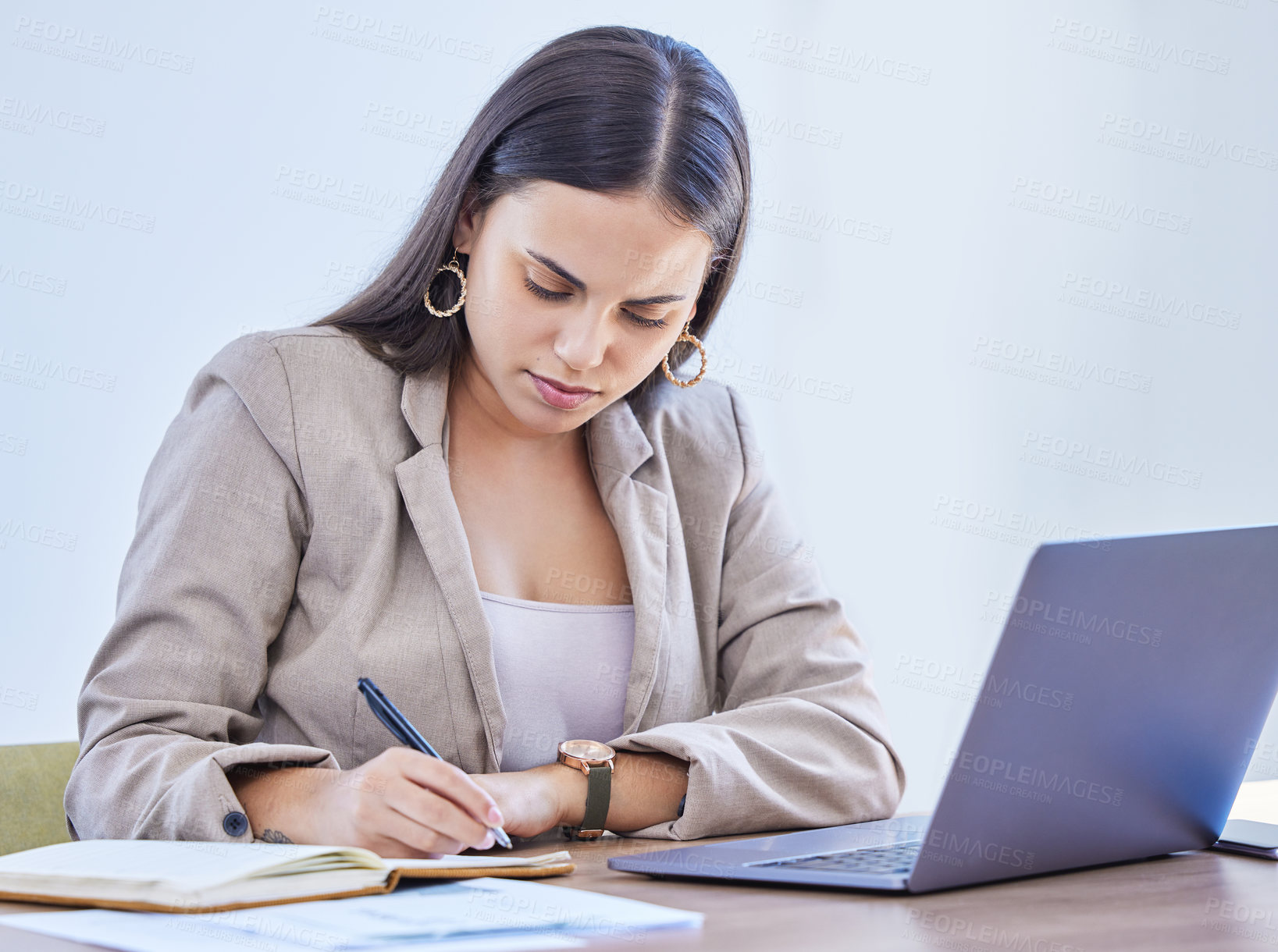 Buy stock photo Shot of a young businesswoman writing notes while working on a laptop in an office