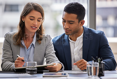 Buy stock photo Shot of two young businesspeople sitting together in the office and having a discussion while using a digital tablet