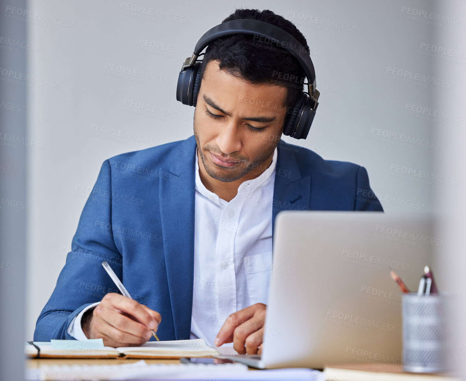 Buy stock photo Shot of a young businessman taking notes while using his laptop