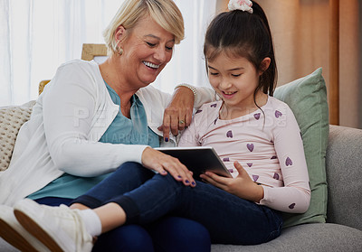 Buy stock photo Shot of an adorable little girl using a digital tablet while sitting at home with her grandmother