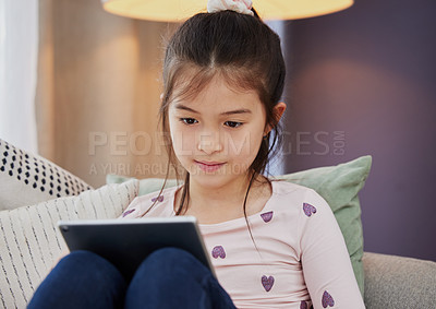 Buy stock photo Shot of an adorable little girl using a digital tablet while sitting at home